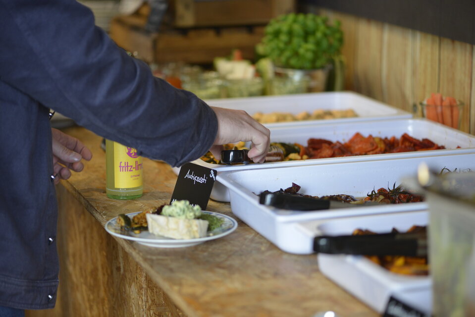 Ein Buffett, im Vordergrund eine Hand, die sich Essen nimmt