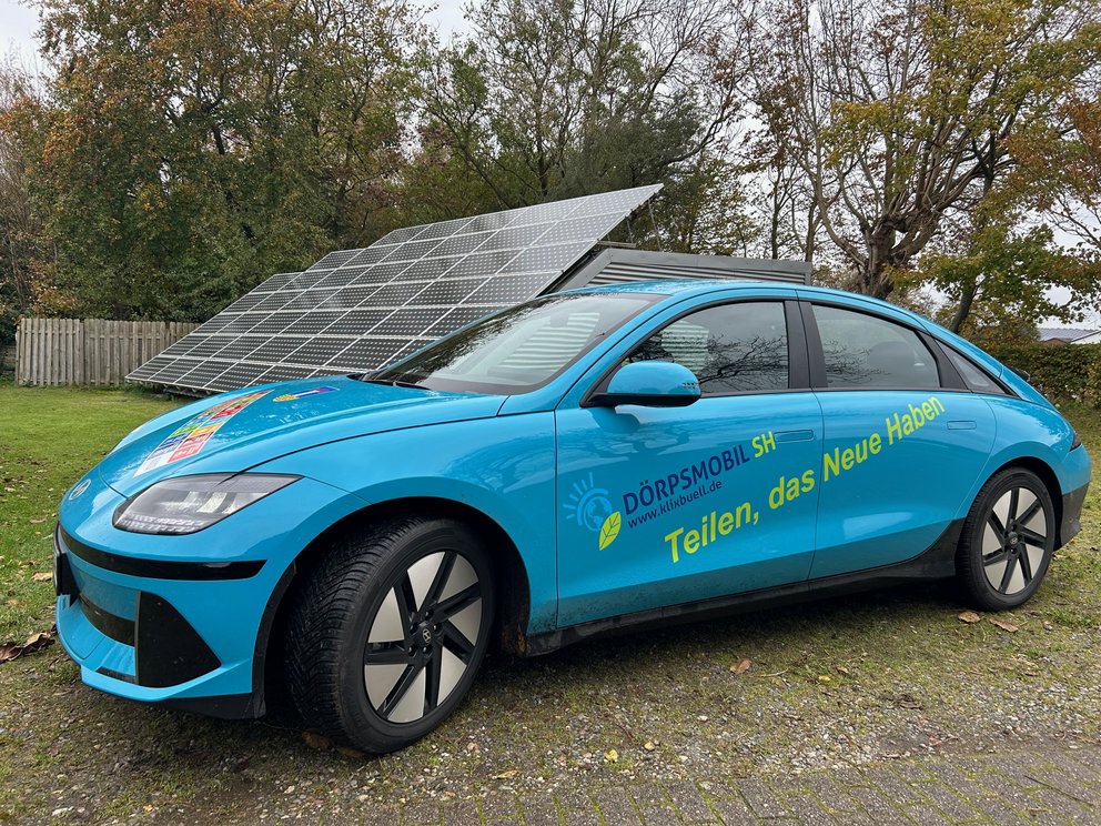Ein blaues Auto mit Elektroantrieb steht vor einer Solaranlage.