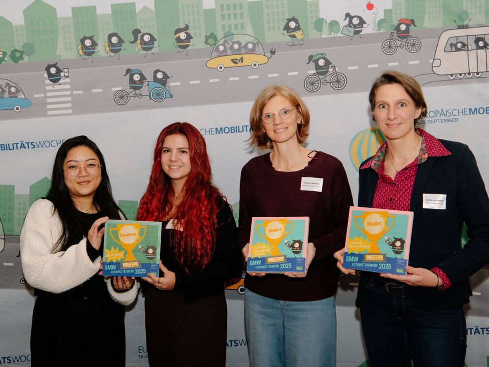 Vier Personen halten drei Urkunden in die Kamera. Im Hintergrund Motive der Europäischen Mobilitätswoche